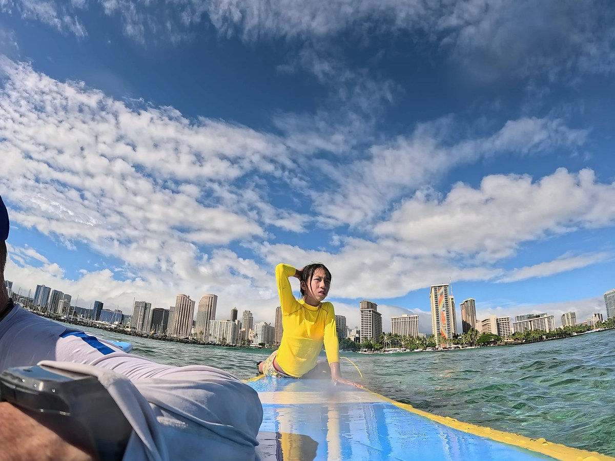 A student rising to their feet on a longboard during an SFC Waikiki lesson