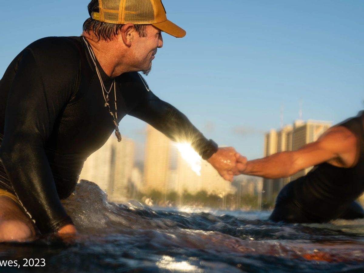 An SFC instructor guiding a surfer in Waikīkī with the shoreline behind them