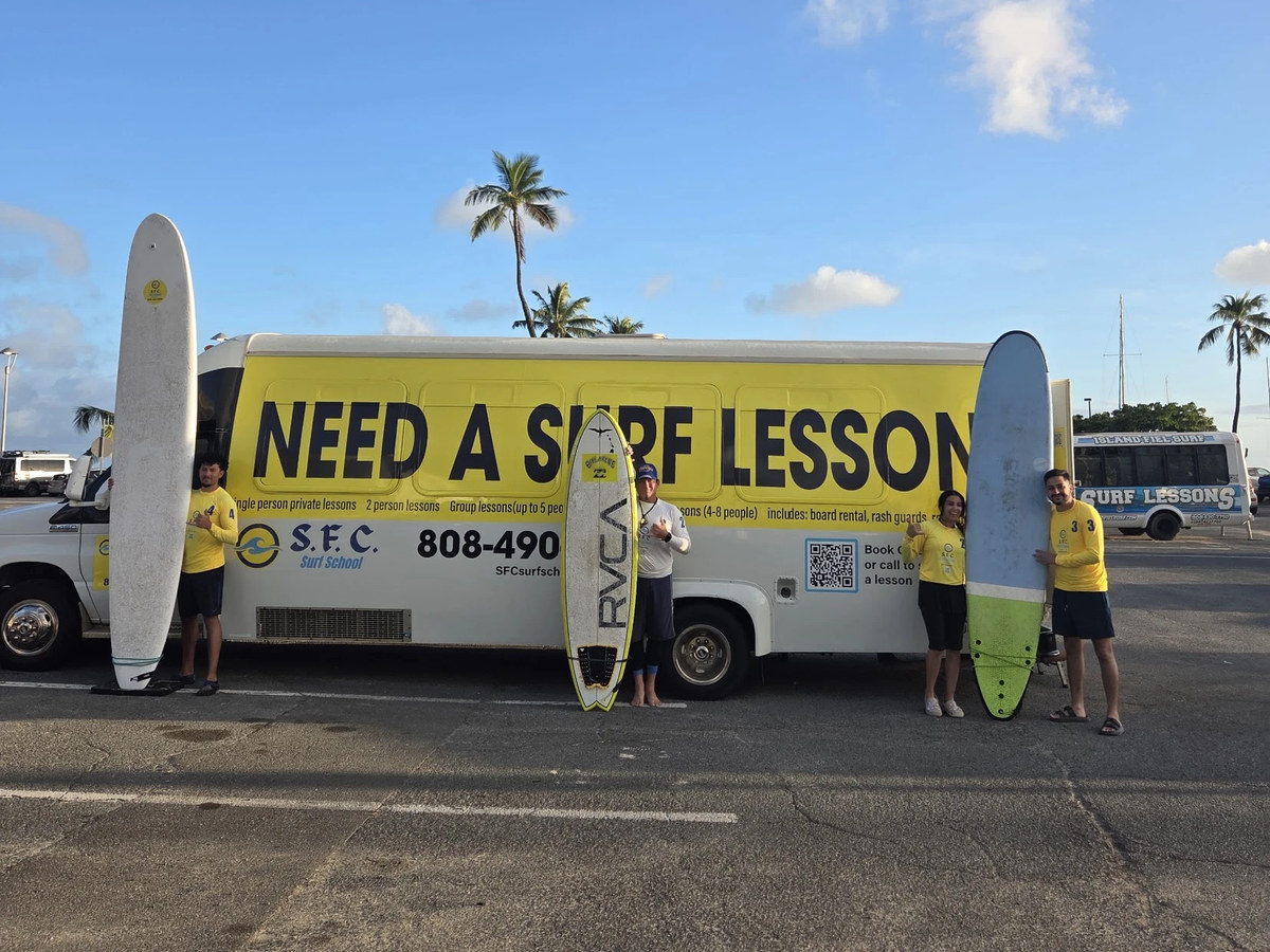 The SFC shuttle bus with three surfers standing in front of it holding boards at Ala Wai Boat Harbor