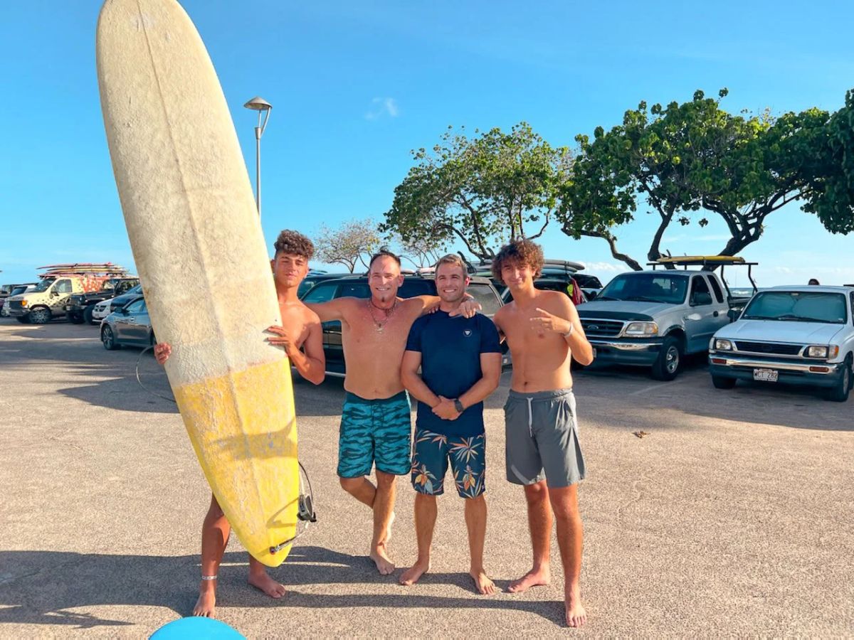 A small group of surfers standing with longboards near the lesson vehicles