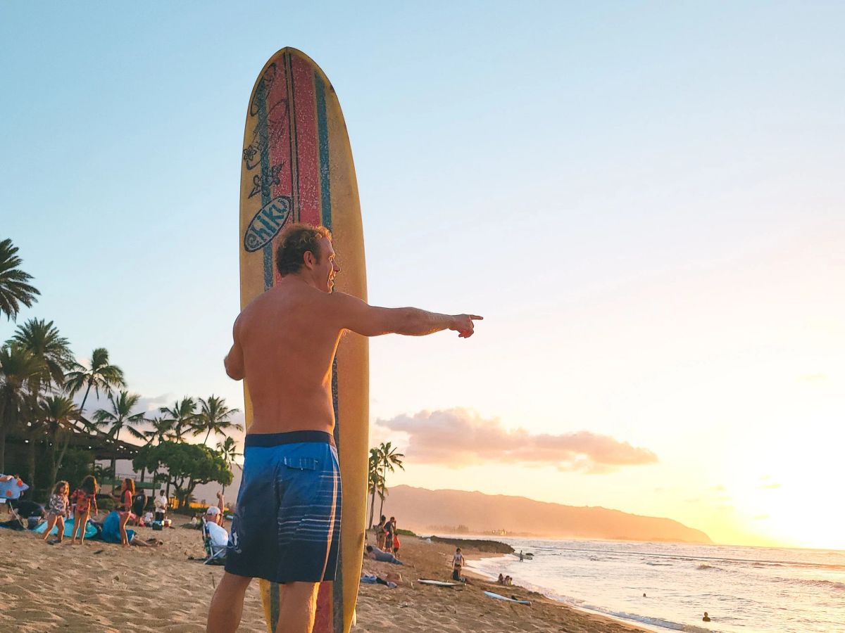 A surfer carrying a longboard beside the water near sunset